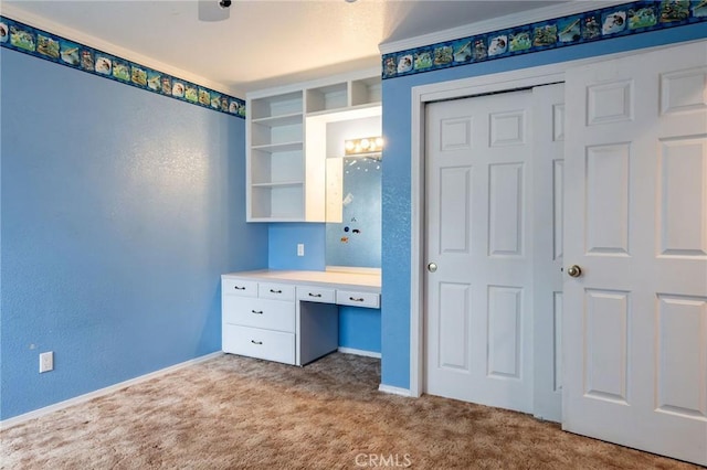 unfurnished bedroom with a textured wall, a closet, baseboards, built in study area, and carpet floors