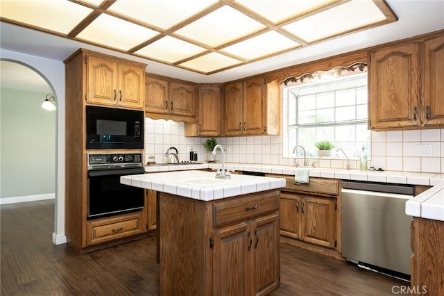 kitchen featuring arched walkways, decorative backsplash, black appliances, dark wood-style floors, and tile countertops