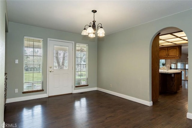foyer entrance featuring baseboards, arched walkways, an inviting chandelier, and dark wood finished floors