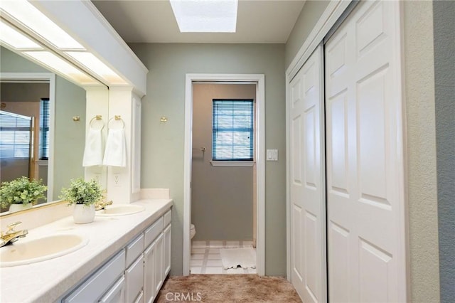 full bathroom with toilet, a skylight, a sink, and double vanity