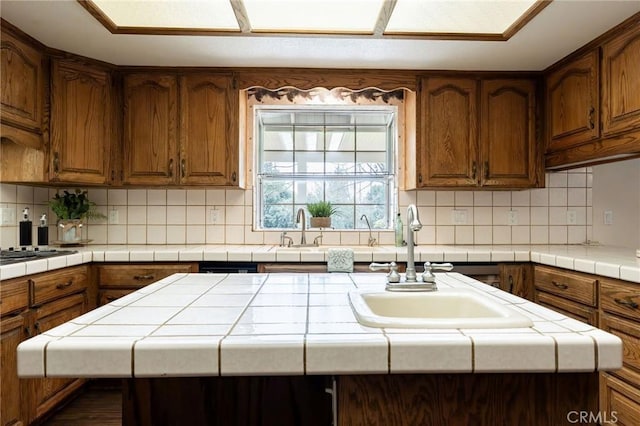 kitchen with tile countertops, decorative backsplash, a kitchen island, and a sink