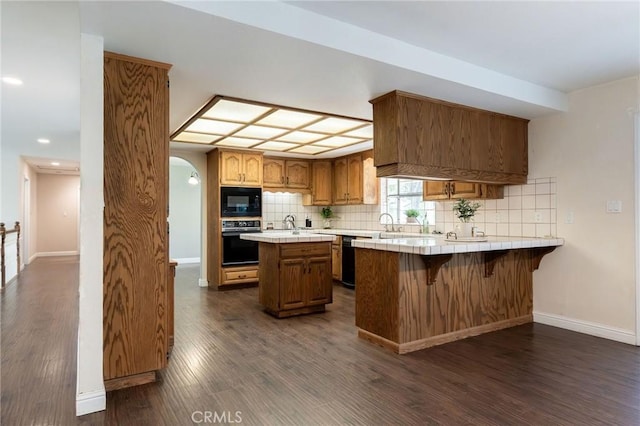 kitchen with tasteful backsplash, black appliances, tile countertops, and dark wood-style flooring