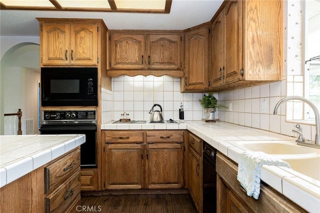 kitchen featuring dark wood finished floors, black appliances, arched walkways, and brown cabinets