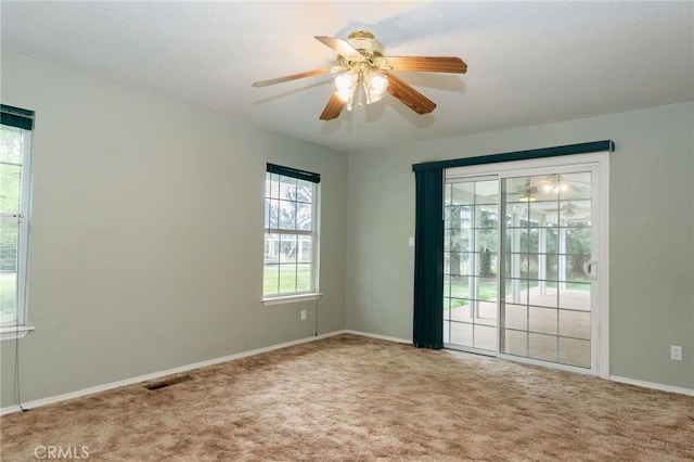 carpeted spare room featuring baseboards, visible vents, a ceiling fan, and a healthy amount of sunlight