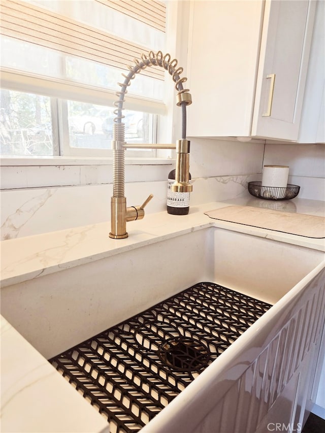 room details with a sink, white cabinets, and light stone counters