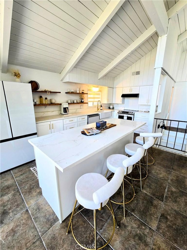 kitchen with lofted ceiling with beams, white cabinetry, stainless steel appliances, and a breakfast bar area