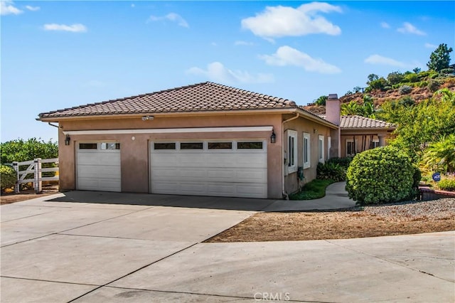 view of front of property with stucco siding, a chimney, driveway, an attached garage, and a tile roof