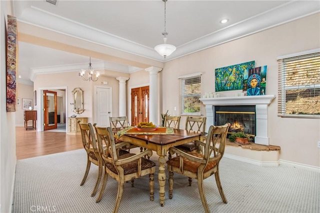 dining area featuring crown molding, ornate columns, a glass covered fireplace, carpet flooring, and baseboards