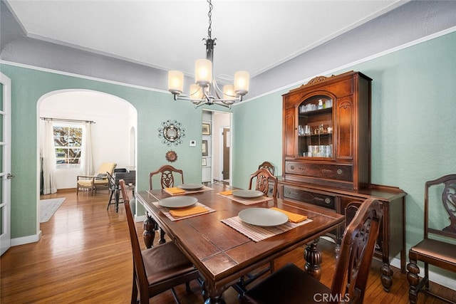 dining room featuring baseboards, ornamental molding, a chandelier, arched walkways, and wood finished floors