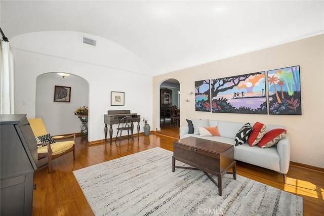 living area featuring arched walkways, wood finished floors, baseboards, and visible vents