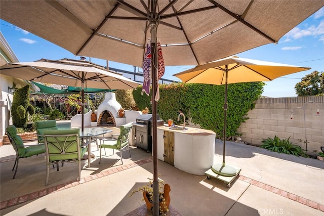 view of patio featuring an outdoor brick fireplace, a sink, grilling area, outdoor dining space, and fence