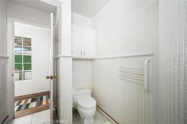 bathroom featuring toilet, tile patterned flooring, and a wainscoted wall