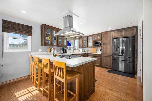 kitchen with visible vents, light countertops, appliances with stainless steel finishes, a peninsula, and island exhaust hood