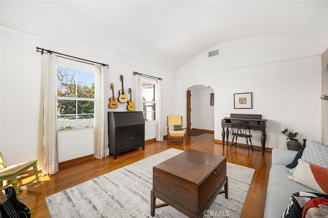 living area with arched walkways, wood finished floors, vaulted ceiling, and visible vents