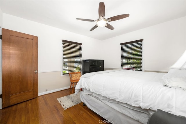 bedroom featuring ceiling fan, multiple windows, baseboards, and wood finished floors