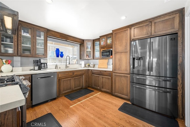 kitchen with light wood-type flooring, glass insert cabinets, light countertops, appliances with stainless steel finishes, and a sink