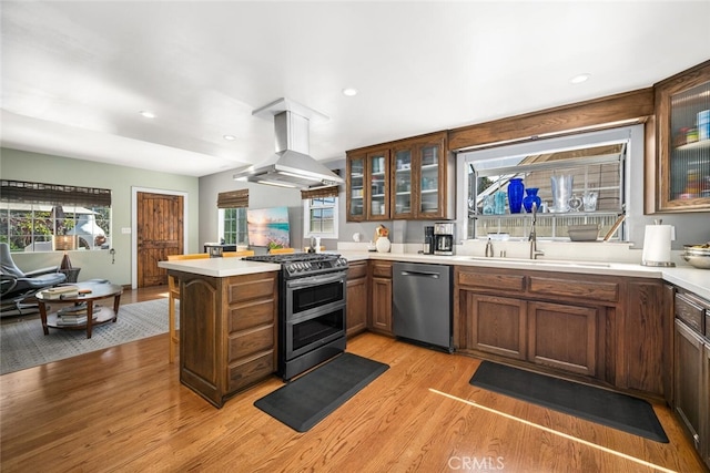 kitchen featuring island exhaust hood, a peninsula, light wood-style flooring, stainless steel appliances, and a sink