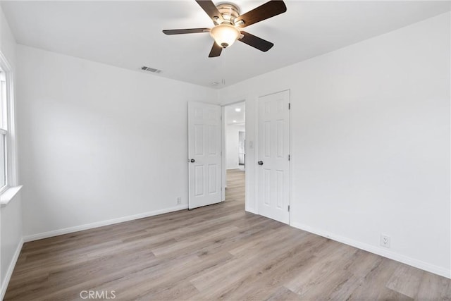 spare room featuring ceiling fan, visible vents, baseboards, and wood finished floors