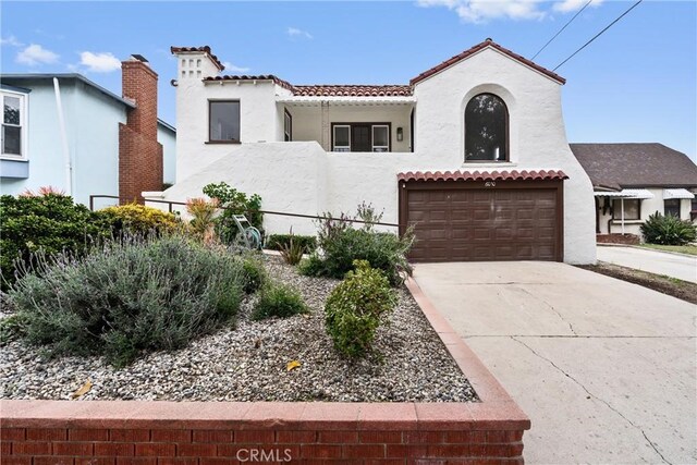 mediterranean / spanish-style home featuring an attached garage, a tiled roof, driveway, and stucco siding