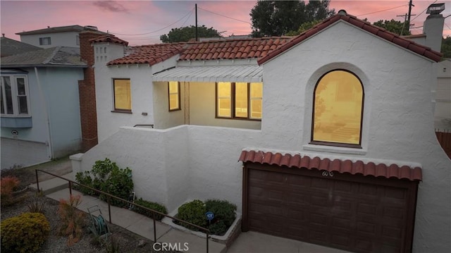 mediterranean / spanish house featuring an attached garage, a chimney, stucco siding, and a tile roof