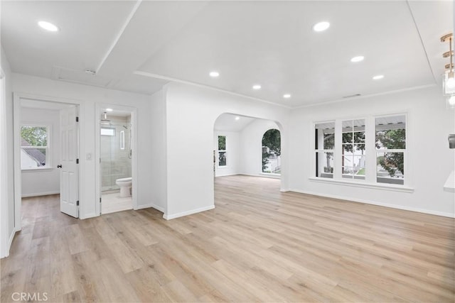 unfurnished living room with recessed lighting, arched walkways, light wood-style floors, and baseboards