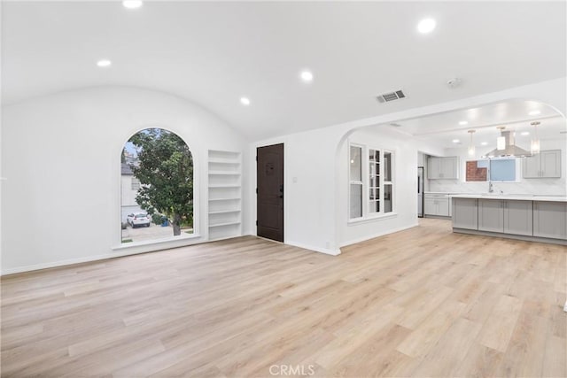 unfurnished living room with visible vents, built in shelves, light wood-type flooring, and arched walkways