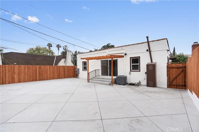 rear view of house featuring central air condition unit, stucco siding, a patio area, fence, and a gate