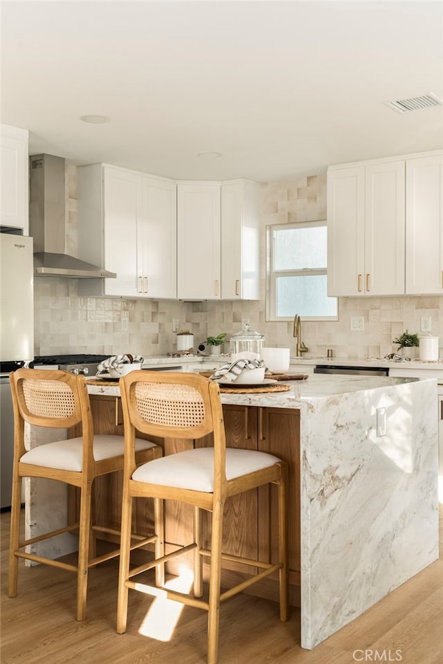 kitchen with wall chimney range hood, backsplash, appliances with stainless steel finishes, and light wood-type flooring