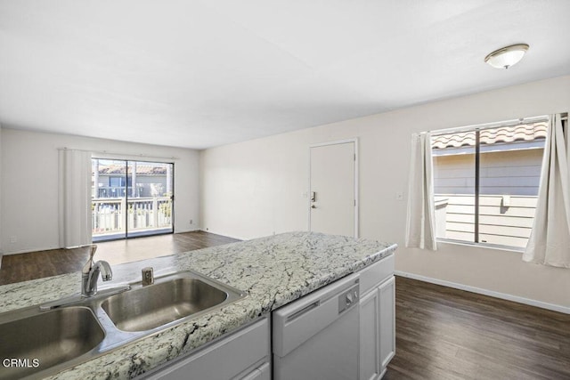 kitchen with a sink, light stone countertops, stainless steel dishwasher, dark wood-style floors, and baseboards