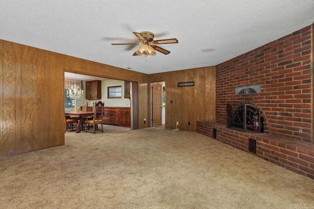 living area featuring wood walls, carpet flooring, a brick fireplace, and ceiling fan with notable chandelier