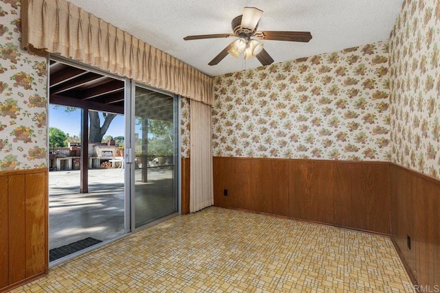 unfurnished room featuring wooden walls, a textured ceiling, wainscoting, and wallpapered walls