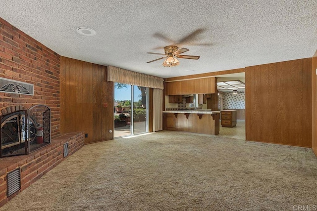 unfurnished living room featuring wood walls, ceiling fan, a brick fireplace, and light carpet