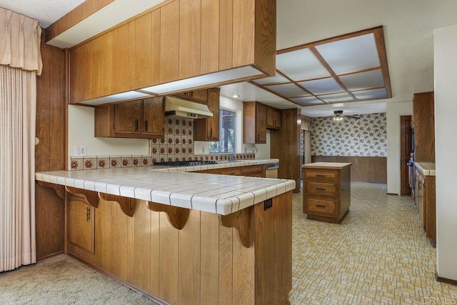 kitchen featuring brown cabinetry, a peninsula, gas stovetop, a breakfast bar, and under cabinet range hood