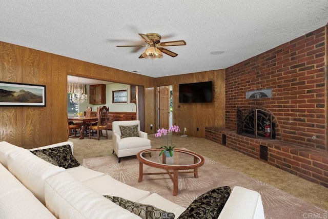 carpeted living area featuring wood walls, a brick fireplace, ceiling fan with notable chandelier, and a textured ceiling