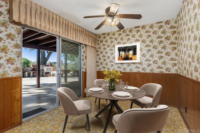 dining room with wooden walls, a textured ceiling, wallpapered walls, and a wainscoted wall