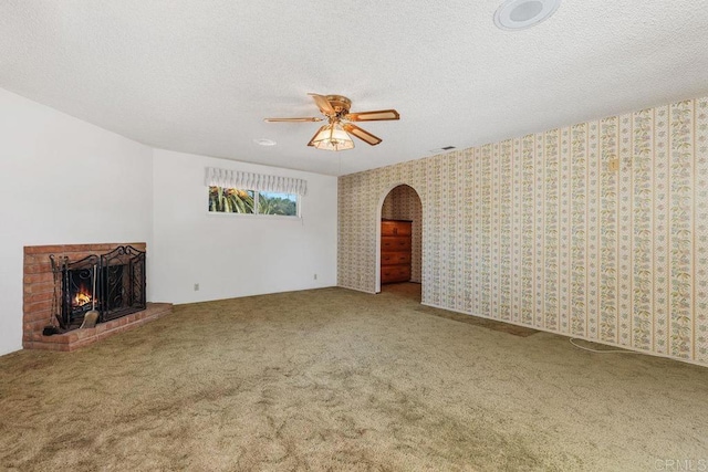 unfurnished living room featuring ceiling fan, a fireplace, arched walkways, a textured ceiling, and carpet floors