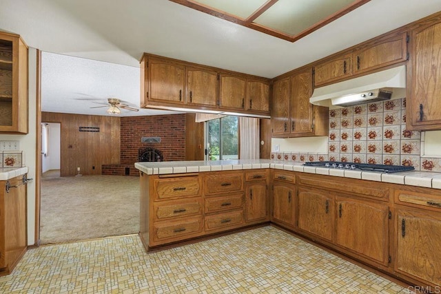 kitchen featuring open floor plan, a ceiling fan, gas cooktop, under cabinet range hood, and brown cabinets