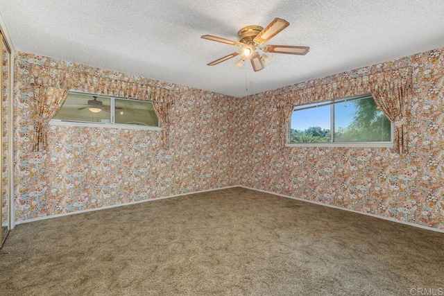 empty room featuring baseboards, ceiling fan, carpet, a textured ceiling, and wallpapered walls