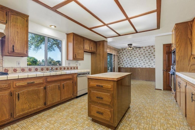 kitchen with white dishwasher, brown cabinets, oven, and a wainscoted wall