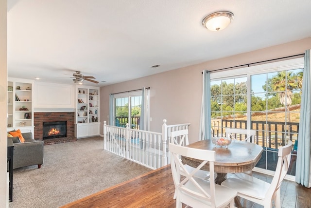 dining space featuring a fireplace, built in features, a ceiling fan, and wood finished floors