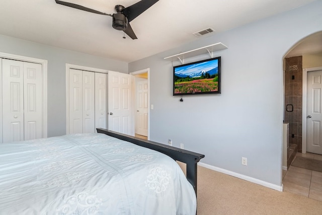 bedroom featuring arched walkways, visible vents, light colored carpet, and multiple closets