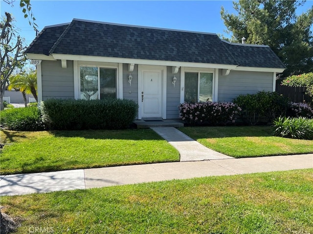 view of front of property with mansard roof, roof with shingles, and a front lawn