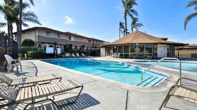 community pool with a sunroom, fence, and a patio area