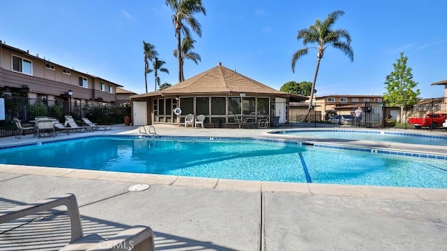 pool with fence, a patio area, and a sunroom