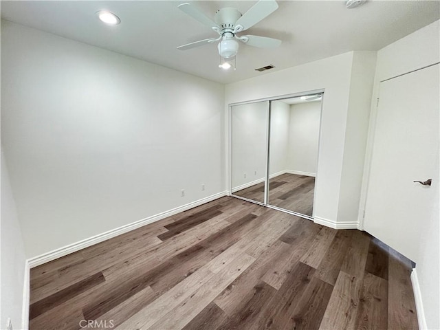 unfurnished bedroom featuring ceiling fan, visible vents, wood finished floors, baseboards, and a closet