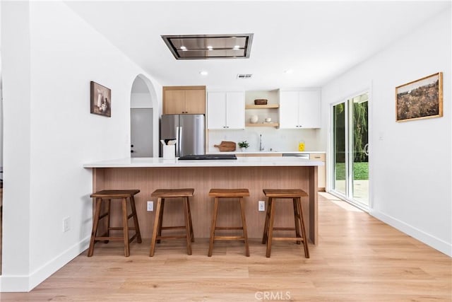 kitchen featuring stainless steel refrigerator with ice dispenser, light wood-style floors, a peninsula, and light countertops