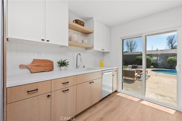 kitchen with open shelves, a sink, light countertops, white dishwasher, and light wood-type flooring