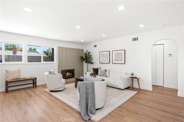 living area featuring a brick fireplace, arched walkways, visible vents, and light wood-style floors