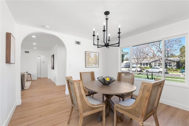 dining area featuring visible vents, light wood-type flooring, baseboards, and arched walkways
