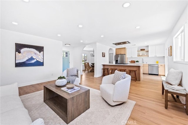 living area with light wood-style floors, recessed lighting, baseboards, and arched walkways